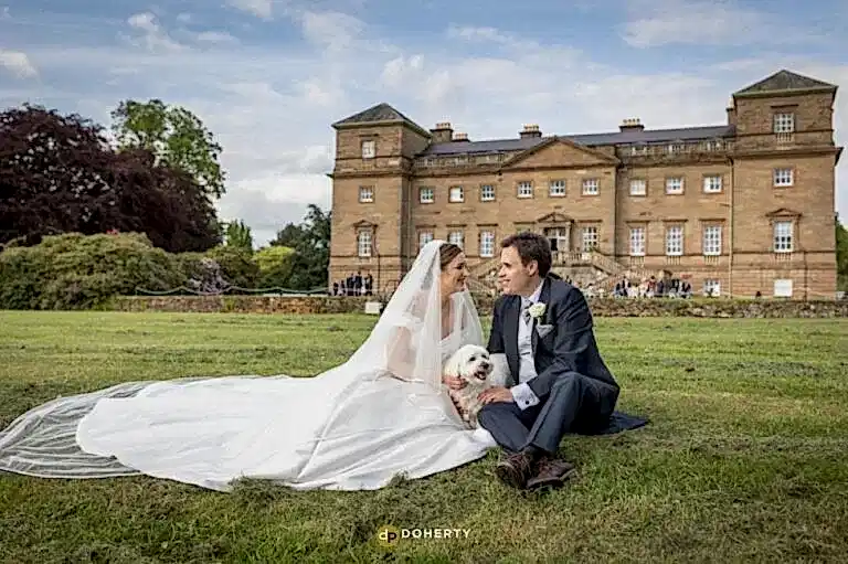 Bride and groom with dog sitting in grounds at Hagley Hall